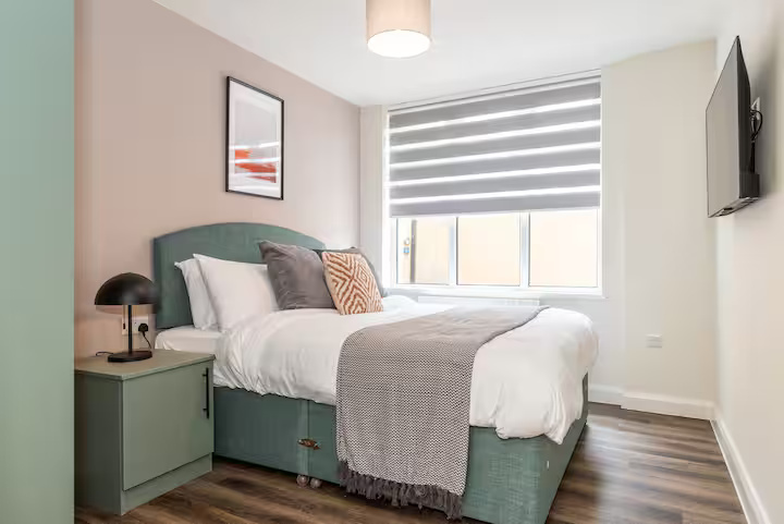 Bright, modern bedroom with comfy double bed, wall television, mushroom-shaped lamp, and laminate flooring