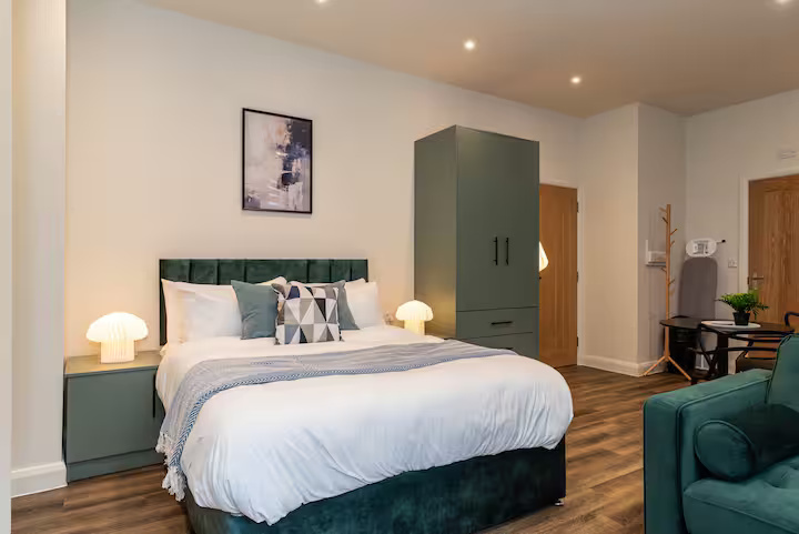 Open, tidy, modern living space featuring a comfy double bed, bedside lamps and cupboards, wardrobe, dining area, inviting sofa, and laminate flooring